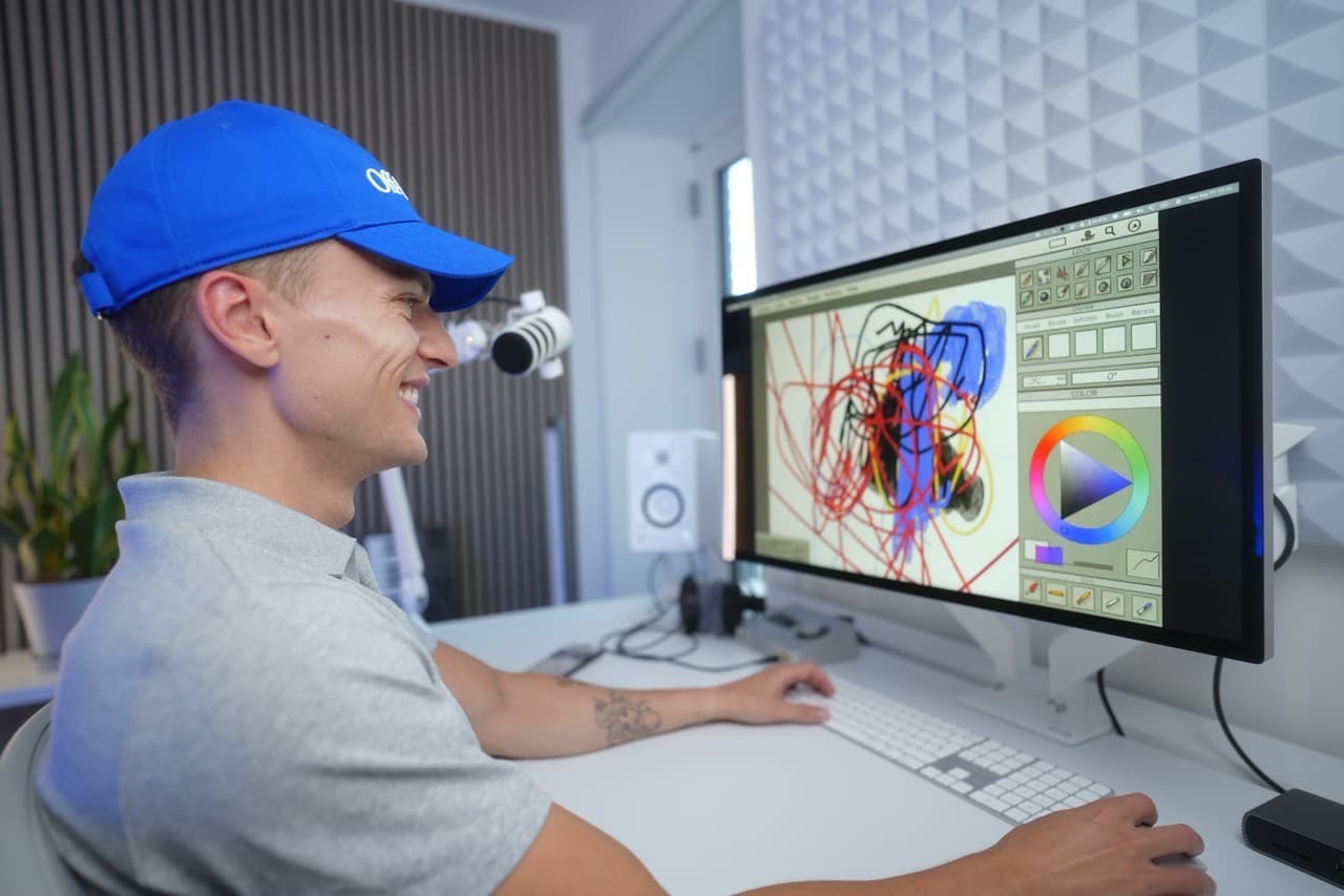 Oliver at his desk in a blue cap, drawing on a large display